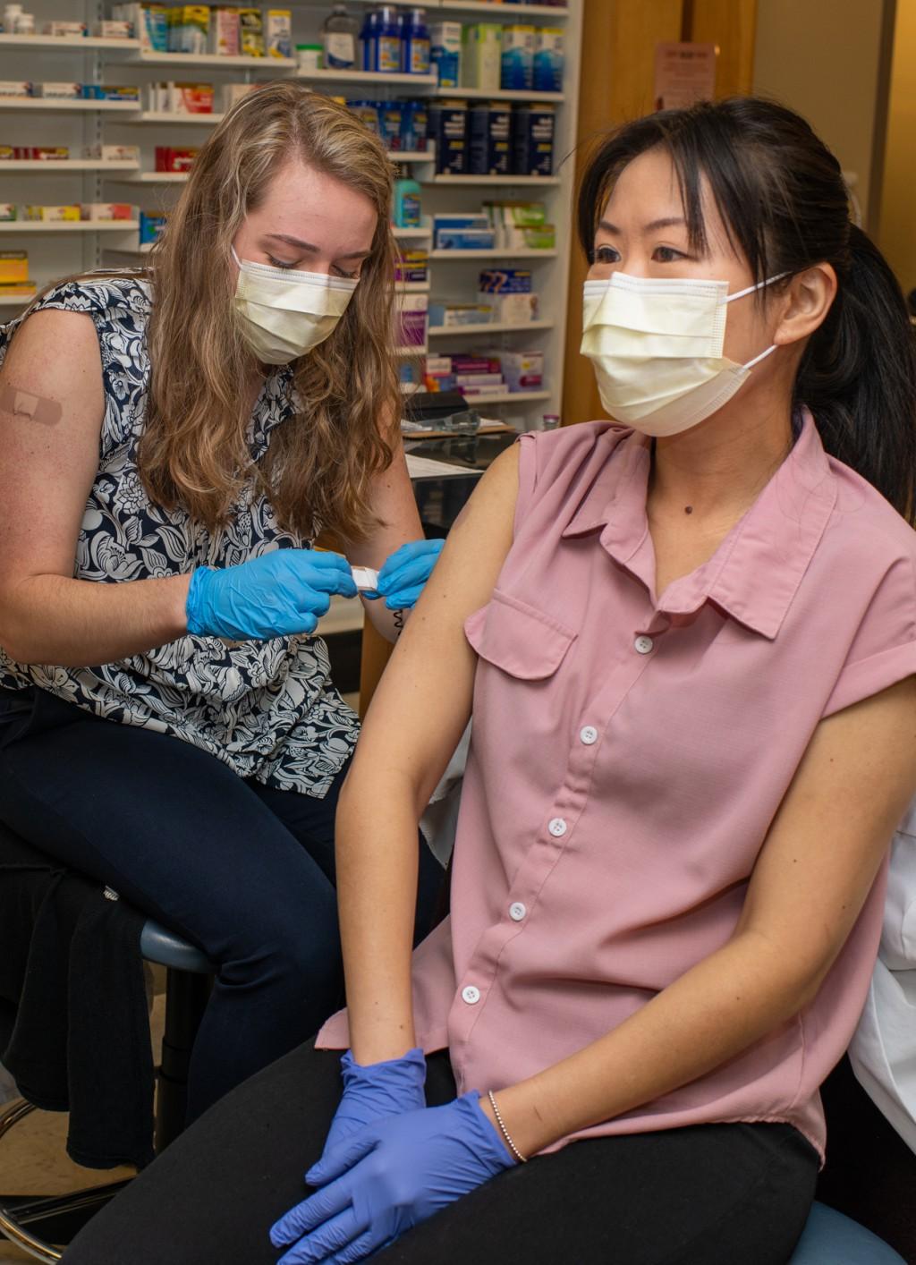 Two pharmacy students are wearing masks and practice giving one another vaccine shots in the upper arm